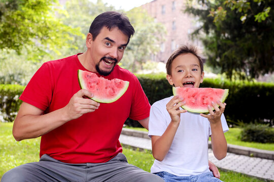 Happy father and son enjoying juicy watermelon in a sunny park. Fun family moment, healthy summer snack, outdoor lifestyle, childhood happiness, and bonding concept