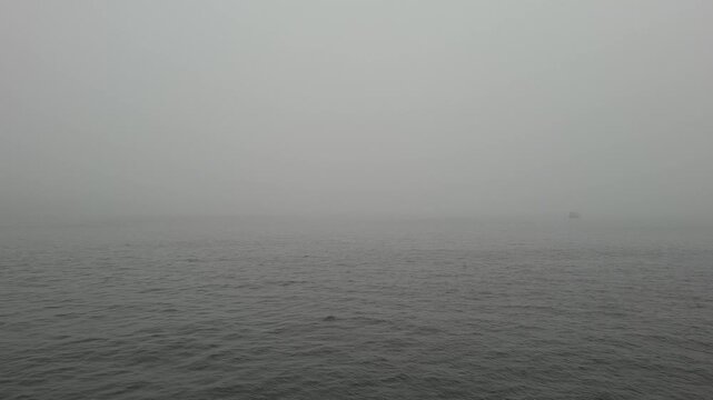 Thick heavy fog rolls over calm sea surface hiding horizon line. Minimalist moody seascape during overcast day. Dark grey water. Dense gray mist envelops quiet ocean, surreal atmospheric background