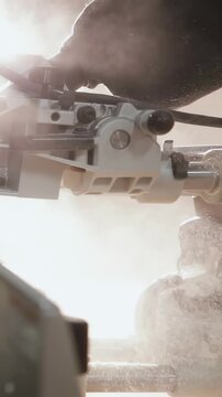 Vertical video: Engaging power, gloved worker lowering miter blade to cut wood in shop with dust