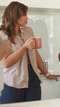 Vertical video: Talking woman in beige top holding pink mug turning with friend speaking at counter