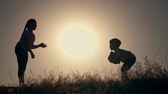 Children playing ball at sunset in nature. Silhouette kids passing ball in scenic sunset. Happy children enjoying nature with ball. Outdoor fun in nature at sunset. Children bonding with ball outdoor.
