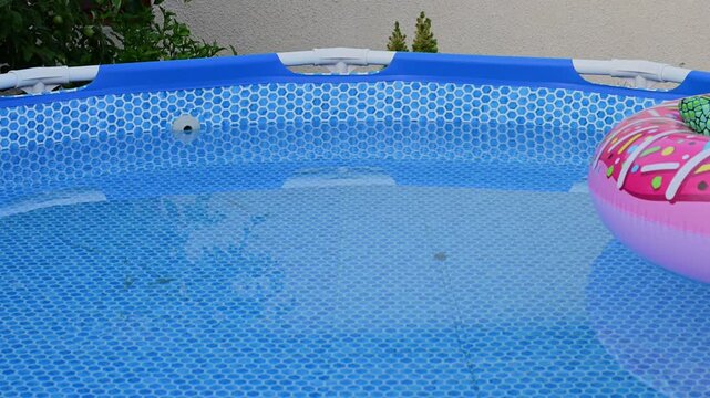 A pink donut-shaped float drifts in a backyard swimming pool.