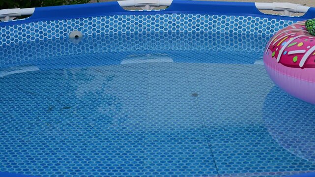 A pink donut-shaped float drifts in a backyard swimming pool.