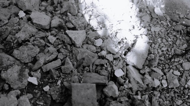 Black and white broken rubble texture with crushed stones, ceramic pieces, harsh light contrast, and construction debris background.
