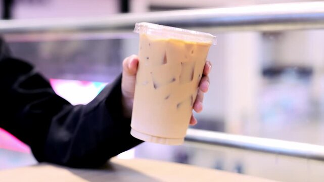 Iced coffee plastic cup hand holding cold beverage drink refreshment urban background creamy cold drink with ice casual summer drink to go plastic container transparent lid urban setting