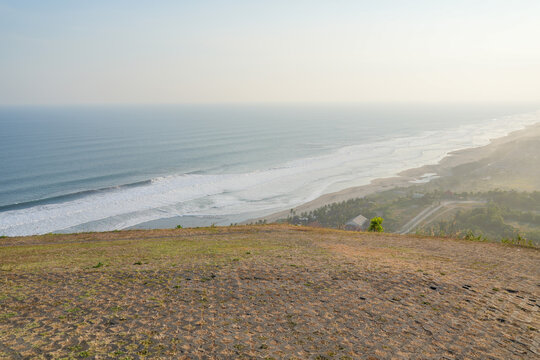 Beautiful views from a high vantage point of the misty coastline with ocean waves crashing onto the sandy beach at sunset.