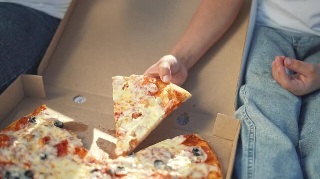 Two children eating pizza outdoors. Siblings enjoying pizza on a sunny day in park. Happy children savoring slice of pizza during family picnic. Carefree childhood moment. Kids eating pizza outdoors.