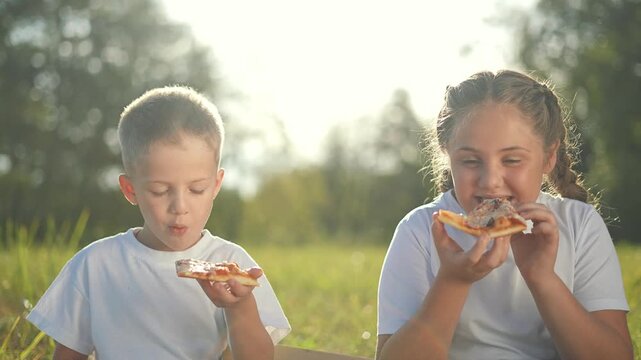 Two kids from same family eating pizza outdoors. Siblings enjoying pizza slice on sunny day. Family picnic with pizza in nature. Happy children sharing pizza outdoors. eating family bonding time.