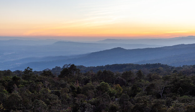 Phu Ruea National Park in Thailand at sunrise. Layered mountains and dense forest landscape. Morning fog and soft light across the hills.