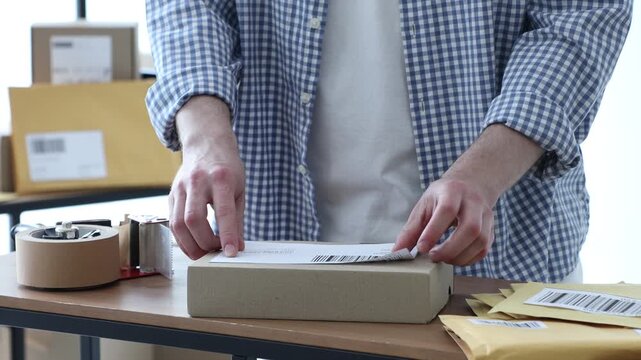 Man sticking barcode onto parcel at table in office, closeup