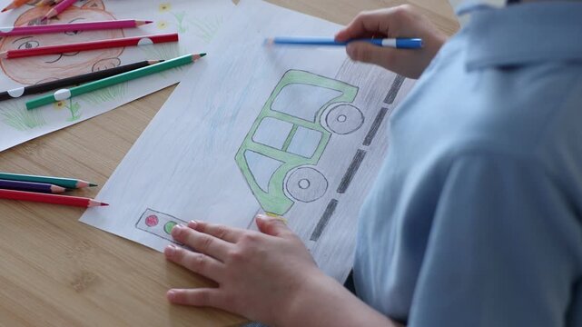 Little boy drawing picture with pencil at wooden desk indoors, closeup