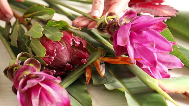 Woman with bouquet of tropical flowers at white wooden table, closeup