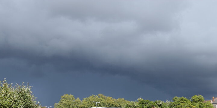 Menacing dark thunderstorm cloud passing by over the tree horizon from left