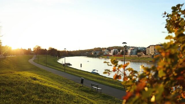 A serene sunset scene featuring a bridge over a pond in a park surrounded by trees and grass. The wide-angle shot captures the tranquil atmosphere with a low-angle perspective, emphasizinga.