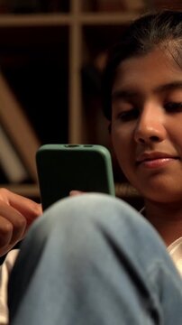 Indian Teenage Girl Using Smartphone While Sitting Comfortably on a Bean Bag at Home with Moody Lighting Against Brick Wall, Scrolling or Staying Connected with Friends Through Social Media