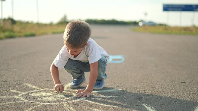 Child drawing with chalk pavement. Kid creates bright sun art outdoors. Happy child focused on creative chalk drawing. Fun summer day activity on pavement. Child enjoys drawing with chalk on pavement.
