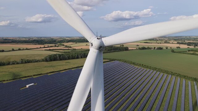 Wind Turbine Spins Above Vast Solar Panel Field in Daylight