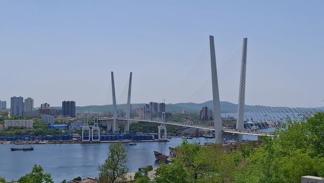 Panoramic view of majestic Zolotoy Bridge in Vladivostok. Iconic cable-stayed structure over Golden Horn Bay. Urban coastal architecture, port facilities, clear blue sky. Beautiful maritime scenery