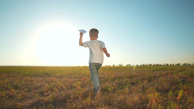 Child running with paper toy at sunset. Boy hand holds paper toy airplane, playing in golden field. Joyful child imagines flight adventure. Sunset glow enhances child dream. Paper toy, child outdoors.