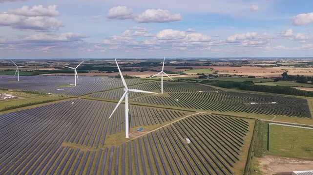 Fields Covered by Solar Panels and Spinning Wind Turbines on a Bright Day