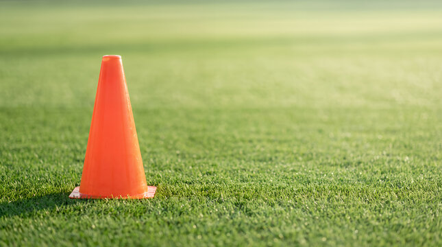 Bright orange training cone on a green grass field with soft morning sunlight