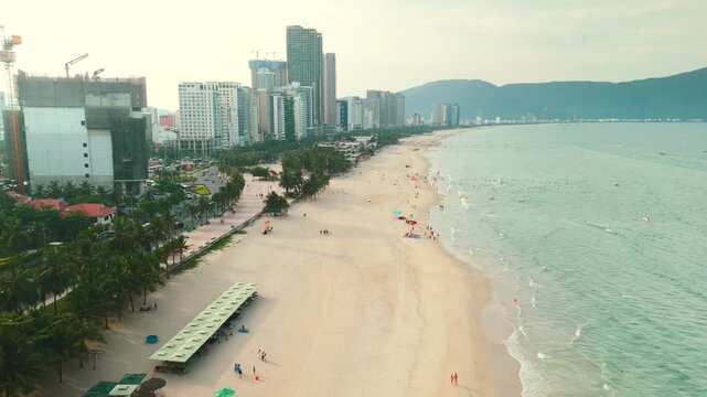 Danang cityscape with my khe beach coastline and vibrant ocean, showcasing urban development, bustling beach activity, and tropical palm tree lined promenades under a bright sky