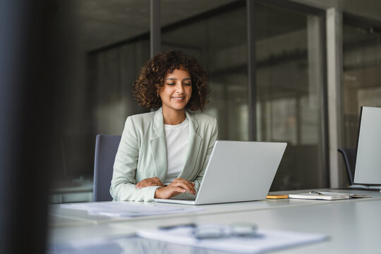 Young professional specialist latin hispanic businesswoman in suit working on laptop pc sitting at desk in office. Middle eastern indian woman using computer technology app for work online. Copy space