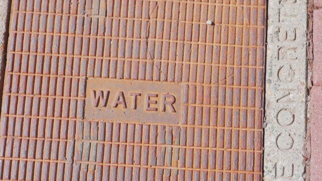 Rusted iron water utility hatch cover on city sidewalk