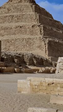 Archaeological site of Saqqara, Egypt, Step Pyramid of Djoser in background with ancient funerary complex ruins, stone blocks and sandy desert foreground.