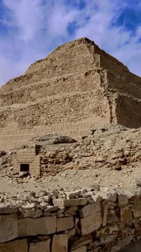 Massive six-stepped limestone pyramid of pharaoh Djoser at Saqqara necropolis, Egypt, with ancient enclosure wall, ruins and sandy desert landscape.
