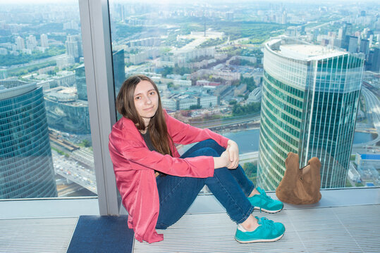 Young woman sitting by panoramic skyscraper window with cityscape view