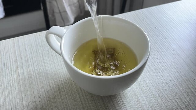 Hot water pouring into a white cup with a tea bag