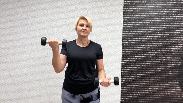 Woman lifts dumbbells for strength training at a fitness center. She focuses on her movements and posture while exercising