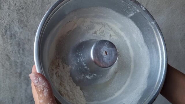 Close-Up of Hand Coating Bundt Cake Pan with Flour to Prevent Sticking Before Baking