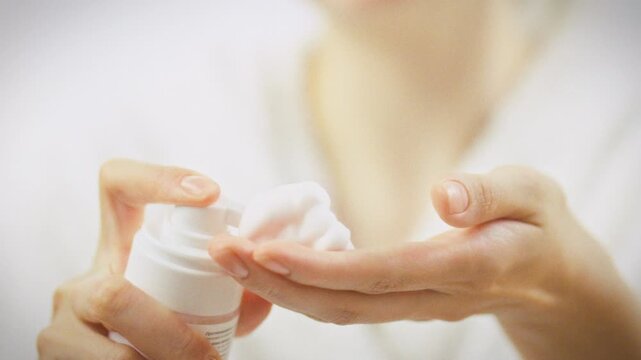 A girl gently squeezes snow-white cleansing foam from a bottle onto her palm, showcasing a daily self-care routine that prioritizes skin health and refreshment with a soothing, airy texture