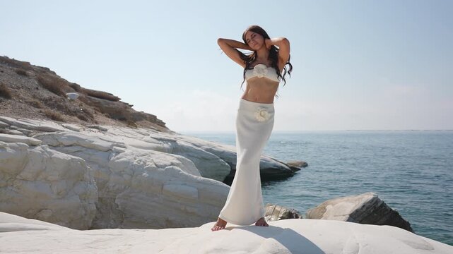 Beautiful young woman posing gracefully on white rocks by the sea