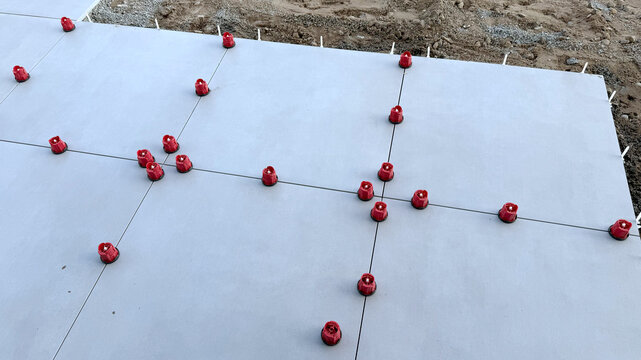 Construction site showing freshly poured concrete slab with red spacers positioned between joints for tile installation