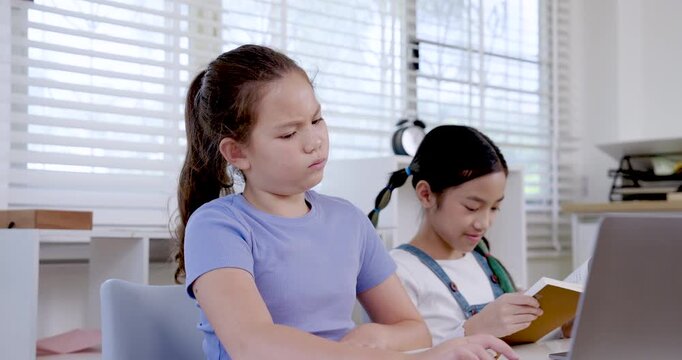 Caucasian preteen girl reading folder beside asian girl working on laptop in classroom representing collaboration digital learning teamwork project education study productivity communication