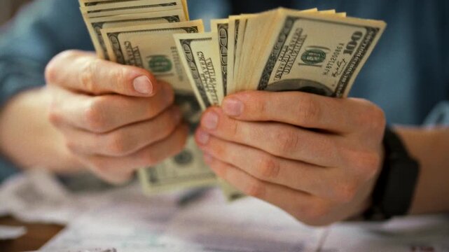 A man sits at a desk, meticulously counting cash while referring to detailed charts and notes, demonstrating his commitment to financial literacy and effective money management skills