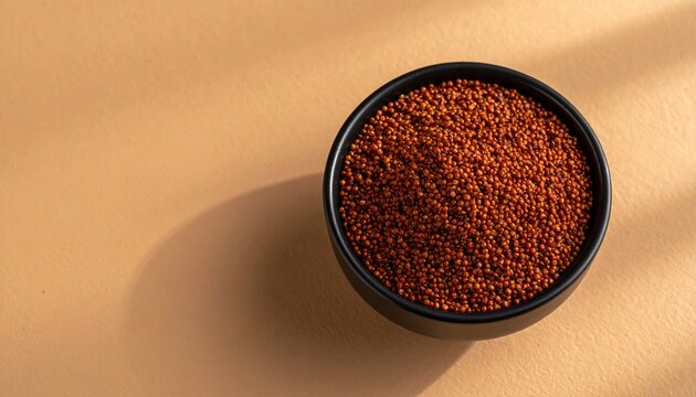 Raw red finger millet ragi grains in a black bowl on a beige background