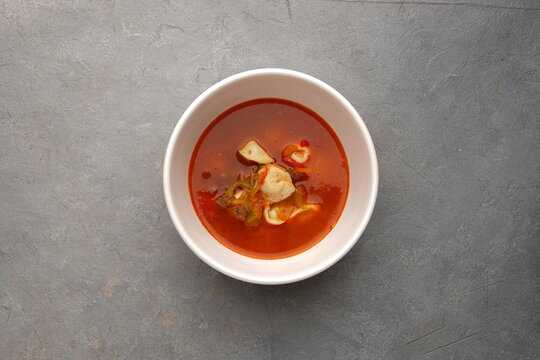 White bowl of spicy red soup with vegetables on gray
