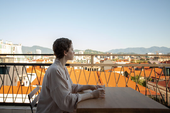 woman recovering from cancer looks across the city from a balcony table with water and medicine, conveying survivorship, quiet reflection and ongoing healthcare