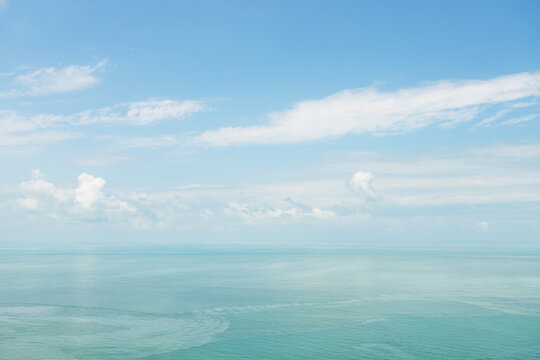 calm black sea horizon beneath a soft blue sky with white clouds, creating an airy coastal background for summer travel, wellness, relaxation and peaceful escape concepts