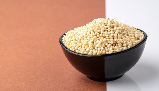 Raw sorghum jowar grains heaped in a black bowl on a dual-tone background