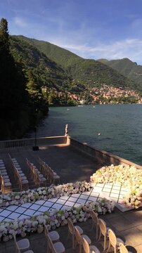 Luxury destination wedding setup on Lake Como with a white aisle leading to a floral arch. Guest seating arranged facing the lake and mountains, creating a cinematic Italian ceremony view.