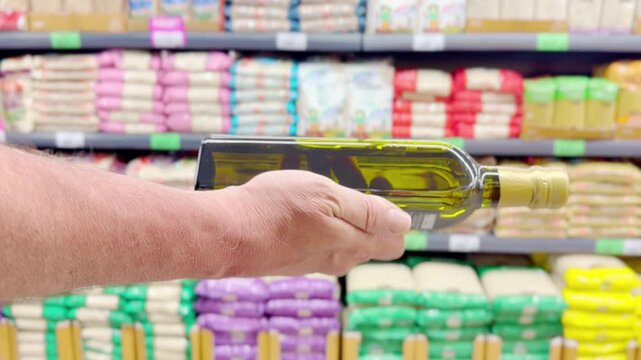 Male Hand Holding a Bottle of Vegetable Oil in Front of Shelves with Various Cooking Oils in a Supermarket