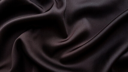 Fototapeta premium Dark brown satin fabric with flowing folds creating luxurious textile background in close up. Elegant cloth texture, glossy material, fashion textile, abstract surface.