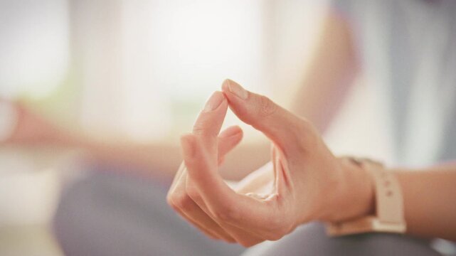 Girl sits in lotus position on yoga mat, practicing mindful meditation with mudra gesture. Embracing yoga's harmony of body mind, she finds inner peace at home on sunny day, cultivating mindfulness