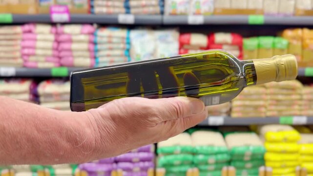 Male Hand Holding a Bottle of Vegetable Oil in Front of Shelves with Various Cooking Oils in a Supermarket