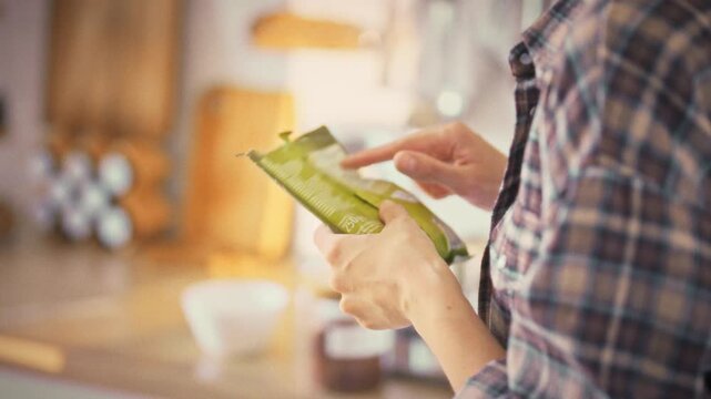In a bright home kitchen, a young woman meticulously examines the label on a soft package, ensuring informed choices about nutrition and healthcare through careful product composition analysis